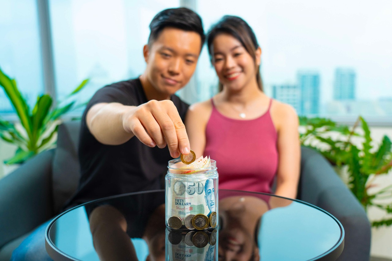 a young couple putting their money in a jar