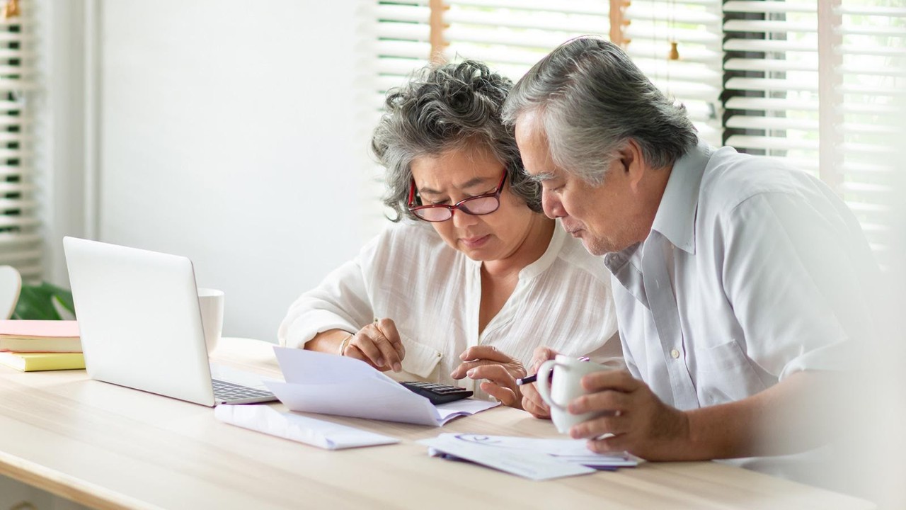 Elderly couple man and woman doing calculations with a stack of papers and a laptop