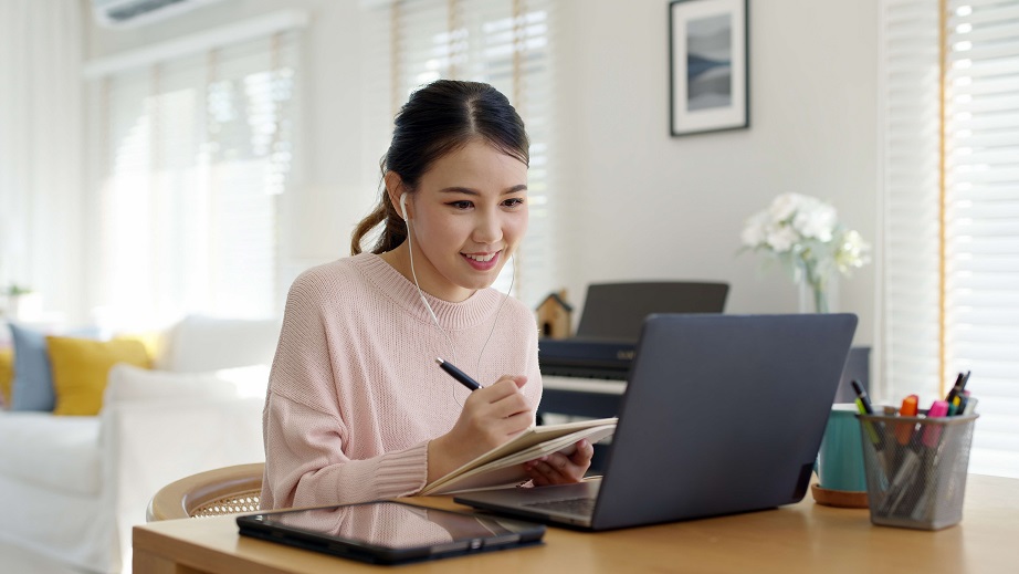 Young lady looking at laptop and taking down notes