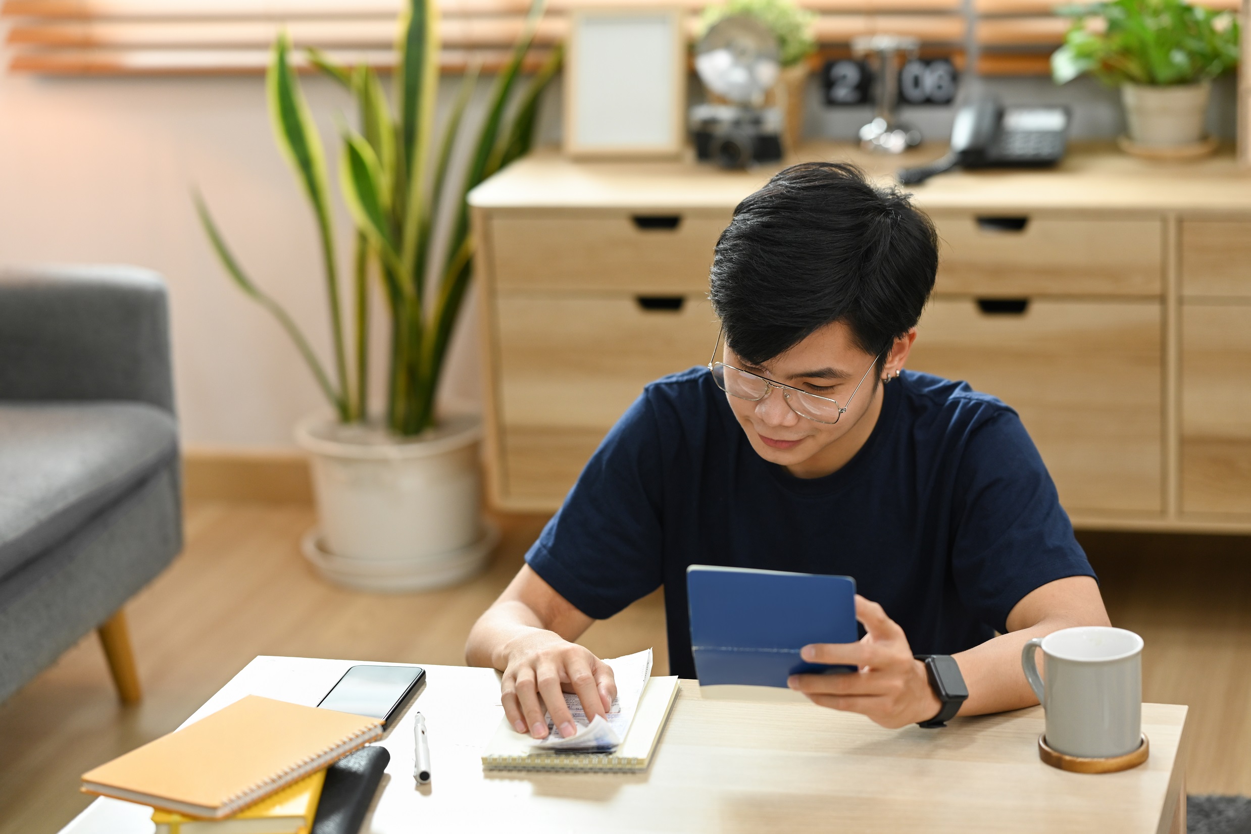 young asian man using device to calculate his expenses at home