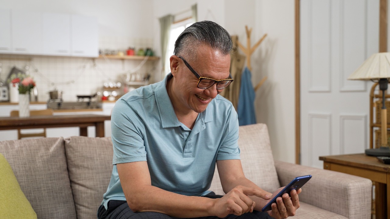 Senior man smiles while scrolling through phone at home